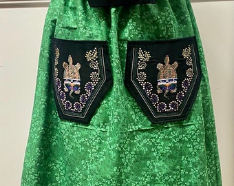 Può includere: Una gonna verde con motivo floreale e una borsa in velluto nero con un disegno di tartaruga. La gonna ha un bordo di nastro verde, viola e blu.
