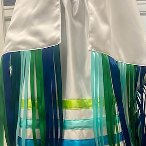 May include: White satin skirt with a green, blue, and turquoise ribbon trim. The skirt has a gathered waistband and a long, flowing design.