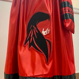May include: A red satin skirt with black ribbon trim and a black and white handprint design. The skirt has a black ribbon sash and a matching pouch.