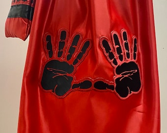 May include: A red satin skirt with black handprint designs. The skirt has a black waistband and a black trim with handprint designs around the bottom.