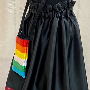 May include: A black skirt with a rainbow trim and a small rainbow-colored bag attached to a black strap. The skirt has a gathered waistband and the bag has a flap closure.
