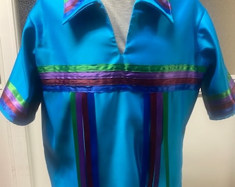 Puede incluir: Una camisa de manga corta azul turquesa con cuello en V. El cuello y las mangas están adornados con cintas multicolores. La camisa tiene una fila de cintas multicolores a través del pecho y una serie de cintas que cuelgan del pecho.
