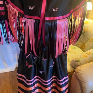 May include: A black satin dress with pink and orange ribbon trim. The dress has a matching black satin shawl with pink ribbon trim and butterfly embroidery.