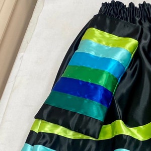 May include: Black skirt with a colorful ribbon detail. The ribbon is made of multiple stripes of green, blue, and yellow satin.
