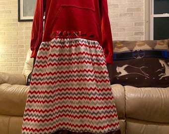 May include: A red hooded sweatshirt with a long, flowing skirt featuring a chevron pattern in red, white, and gray. The skirt has a brown ribbon with a repeating pattern of small red figures.