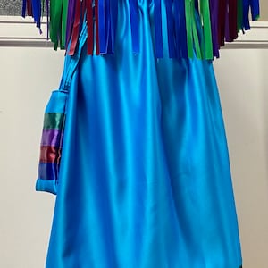 Könnte beinhalten: Ein türkisfarbenes Satin-Kleid mit einem passenden türkisfarbenen Satin-Umhang. Der Umhang hat einen Fransenbesatz aus mehrfarbigen Bändern. Das Kleid hat einen Band aus mehrfarbigen Bändern am unteren Saum.