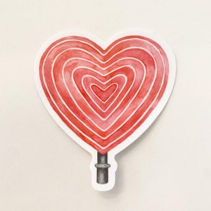 May include: A red heart-shaped lollipop with white stripes. The lollipop is on a stick.