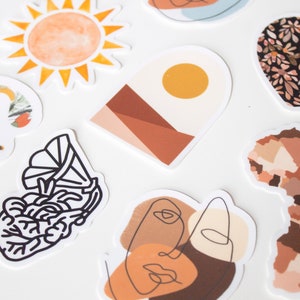 May include: A collection of decorative stickers with various designs. Includes a watercolor sun, a floral letter "C", an abstract landscape, a heart-shaped floral pattern, a line art face, a gramophone, and an African continent map.