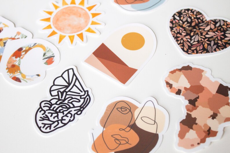 May include: A collection of decorative stickers with various designs. Includes a watercolor sun, a floral letter "C", an abstract landscape, a heart-shaped floral pattern, a line art face, a gramophone, and an African continent map.