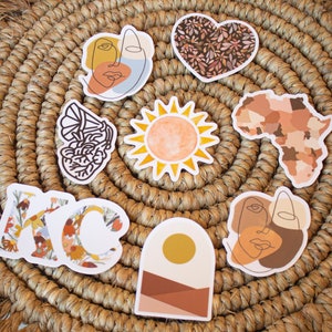May include: A collection of decorative stickers with various designs, including a sun, a heart with floral patterns, an outline of Africa, and abstract face art. The stickers are arranged on a woven, circular placemat.