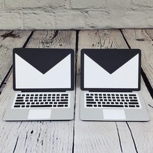 May include: Two closed laptop computers with black screens and white envelopes displayed on the screen. The laptops are on a wooden surface.