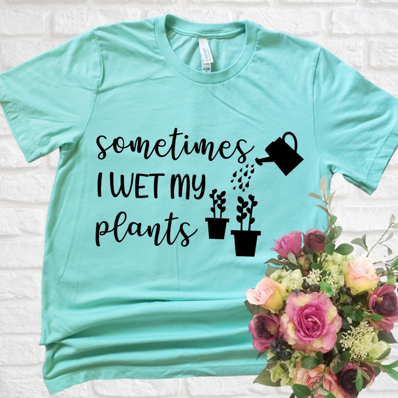 May include: A turquoise blue t-shirt with the text "sometimes I WET my plants" in black lettering. A black watering can is pouring water onto three black potted plants.