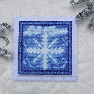 May include: A blue and white cross-stitch design featuring a snowflake with the text "Let It Snow" above it.