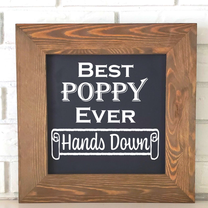May include: A framed chalkboard sign with the text "Best Poppy Ever Hands Down" in white lettering on a dark blue background.