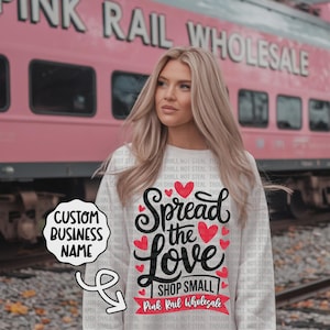Könnte beinhalten: Weißes Sweatshirt mit dem Text "Spread the Love" in schwarzer Schrift und roten Herzen. Der Schriftzug "Shop Small" steht darunter, mit "Pink Rail Wholesale" auf einem roten Banner. Individueller Firmenname möglich.