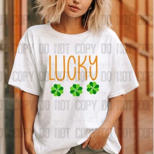 May include: White t-shirt with the word "LUCKY" in orange text and three green four-leaf clovers.
