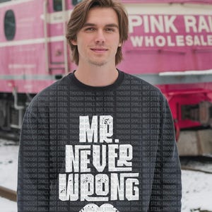 May include: A navy blue sweatshirt with the text "MR. NEVER WRONG" in white, along with a white mustache graphic. The phrase "THOUGH SHALL NOT STEAL" is printed repeatedly around the design. A pink train is in the background.