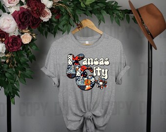 Op de afbeelding: Een grijs T-shirt met een patchwork-ontwerp van de woorden "Kansas City" in een retro-lettertype.