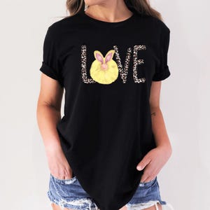 Puede incluir: Camiseta negra con un gráfico de la palabra "LOVE" en estampado de leopardo con un conejito amarillo en el medio de la "O".