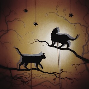 Op de afbeelding: Twee zwarte katten silhouetten zitten op takken van een boom tegen een gouden achtergrond. De katten kijken in verschillende richtingen en zijn zwart omlijnd. De achtergrond is licht goudkleurig met een subtiele textuur. Kleine zwarte sterren hangen aan de takken.