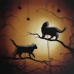Op de afbeelding: Twee zwarte katten silhouetten die op takken van een boom zitten tegen een warme, gouden achtergrond. De takken zijn versierd met hangende sterren, wat een fantasierijke en magische sfeer creëert.