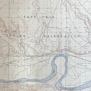 Może przedstawiać: Antyczna mapa rezerwatu Indian Fort Peck w Montanie. Mapa przedstawia topografię obszaru, w tym rzeki, góry i doliny. Mapa jest wydrukowana na kremowym papierze i ma brązową ramkę.