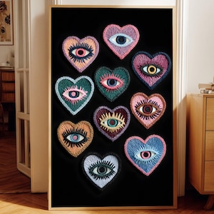 May include: A framed artwork featuring eleven embroidered heart-shaped designs, each with an eye motif. The hearts are in various colors, including pink, blue, orange, and green, set against a black background. The frame is a light wood color.