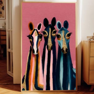 Puede incluir: Una impresión de arte mural vertical enmarcada que presenta tres cabezas de caballo estilizadas sobre un fondo rosa sólido. Los caballos están representados en tonos azul, negro y naranja con acentos texturizados dorados en sus caras y pestañas largas.