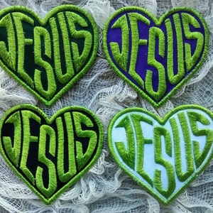 Peut inclure: Quatre patchs en forme de cœur vert avec le mot "JESUS" brodé en blanc. Les patchs sont sur un fond blanc.