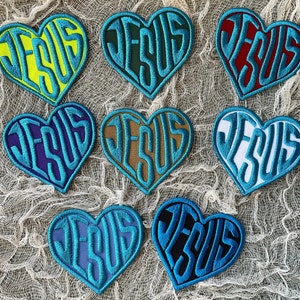 May include: Eight heart-shaped patches with the word "JESUS" embroidered in different colors, including blue, green, yellow, red, purple, brown, white, and black.