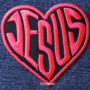 Può includere: Toppa ricamata rosa a forma di cuore con la parola "JESUS" all'interno. La toppa è su uno sfondo di denim blu. L'hashtag #tool4soul è sotto la toppa.