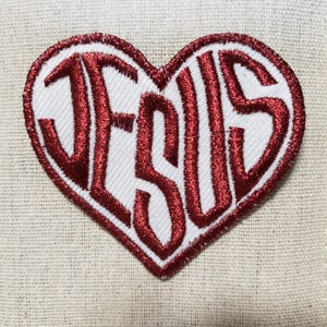 May include: Red embroidered patch in the shape of a heart with the word "JESUS" inside.