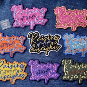 May include: Eight embroidered fabric patches featuring the text Raising Tiny Disciples in various color combinations including pink, orange, gold, blue, yellow, purple, and black. A small square tag labeled Handmade Iron On Patch is included.