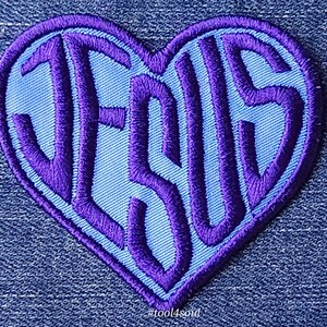 May include: Purple embroidered patch in the shape of a heart with the word "JESUS" in a light blue background. The patch has a hashtag at the bottom that reads "#tool4soul".