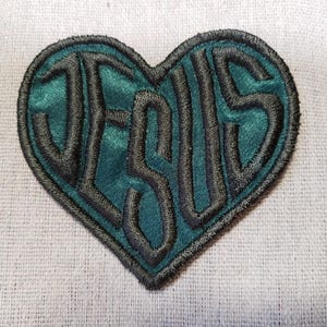 May include: A teal blue and black embroidered patch in the shape of a heart with the word "JESUS" inside.