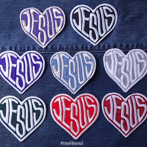 Könnte beinhalten: Neun Bügelbilder in Herzform mit dem Wort "JESUS" darin. Die Patches sind in verschiedenen Farben, darunter Lila, Schwarz, Blau, Grau, Grün und Rot.