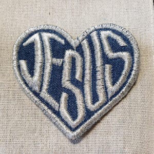 May include: A blue denim heart-shaped patch with the word "JESUS" embroidered in white thread.