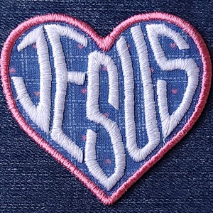 May include: A pink heart-shaped patch with the word "JESUS" embroidered in white on a blue background with white polka dots.