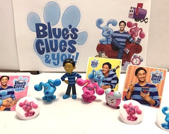 May include: A set of Blue's Clues & You! toys and stickers featuring the characters Blue, Magenta, and the host. The set includes a small blue dog figurine, a small pink dog figurine, a small figurine of the host, and several stickers with images of the characters and the host.
