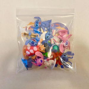 Może przedstawiać: Plastikowa torba wypełniona r&oacute;żnymi małymi plastikowymi figurkami. Figurki przedstawiają Stitch i Angel z filmu Disneya Lilo & Stitch. Figurki są w r&oacute;żnych pozach i noszą r&oacute;żne stroje.
