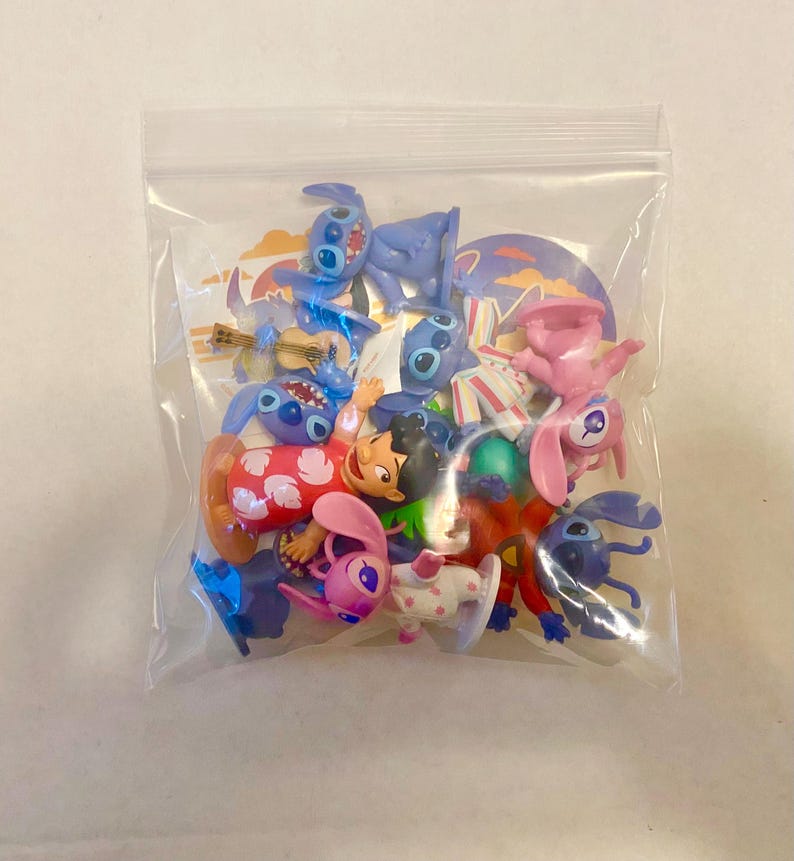 Może przedstawiać: Plastikowa torba wypełniona r&oacute;żnymi małymi plastikowymi figurkami. Figurki przedstawiają Stitch i Angel z filmu Disneya Lilo & Stitch. Figurki są w r&oacute;żnych pozach i noszą r&oacute;żne stroje.