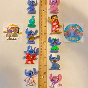 May include: A collection of 10 Stitch figurines, including a pink Stitch, a Stitch playing a guitar, a Stitch wearing a red shirt, and a Stitch wearing pyjamas. The figurines are all about 5 cm tall and are made of plastic. There are also two stickers, one with the text "Aloha!" and the other with the text "CHILL".