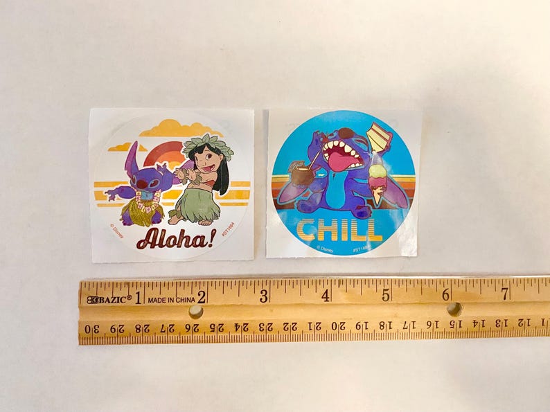 Może przedstawiać: Dwa okrągłe naklejki z Stitch'em z Lilo & Stitch. Pierwsza naklejka jest niebieska z Stitch'em w kwiecistym naszyjniku i napisem "Chill". Druga naklejka jest pomarańczowa i ż&oacute;łta z Stitch'em i dziewczyną w kwiecistych naszyjnikach i napisem "Aloha!"