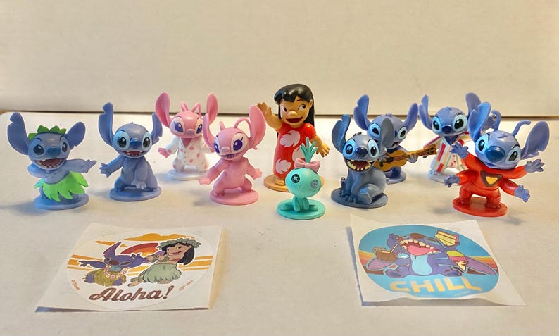 May include: A collection of 10 small plastic figurines of Stitch and his friends from the Disney movie Lilo & Stitch. The figurines are in various poses and include Stitch, Angel, Jumba, and Lilo. There are also two stickers with the words "Aloha!" and "Chill" on them.