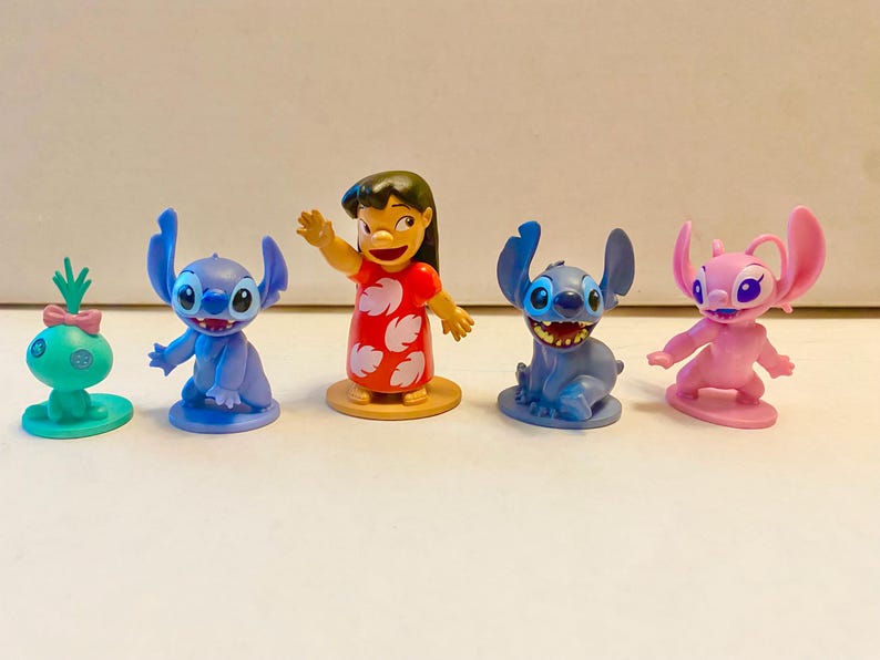 Może przedstawiać: Pięć małych plastikowych figurek postaci z filmu Disneya Lilo & Stitch. Postacie to Stitch, Angel, Lilo i dwie inne wersje Stitcha. Figurki stoją na białym tle.