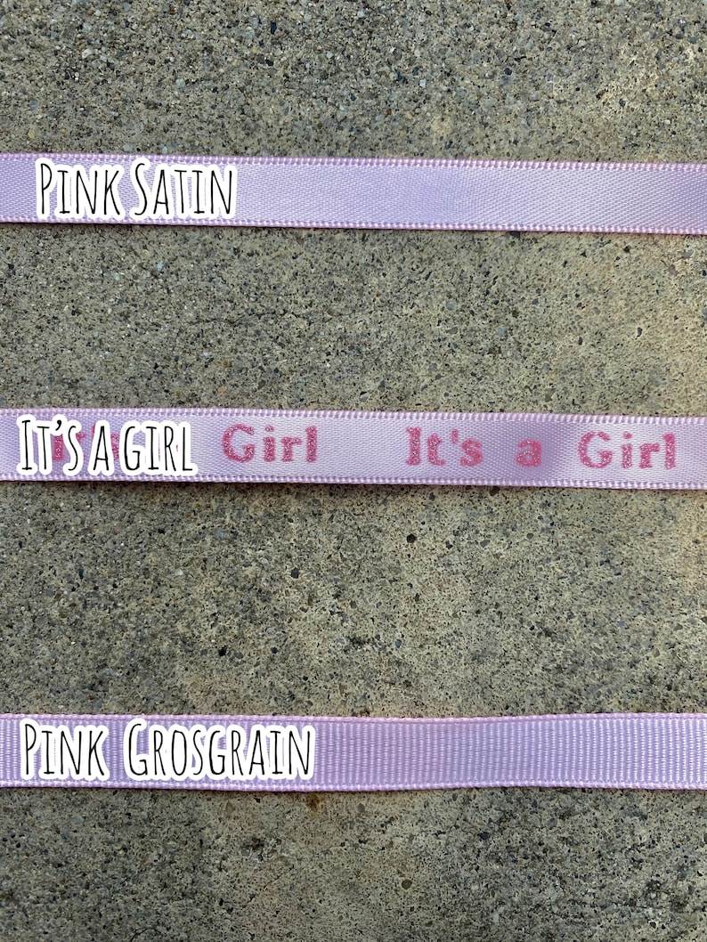 May include: Three ribbons in shades of pink are displayed. The top ribbon reads "PINK SATIN". The middle ribbon has the text "IT'S A GIRL" printed on it. The bottom ribbon reads "PINK GROSGRAIN".