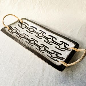 May include: Rectangular serving tray with a black and white chain link design. The tray has a black border and two woven handles. The tray is on a white surface.