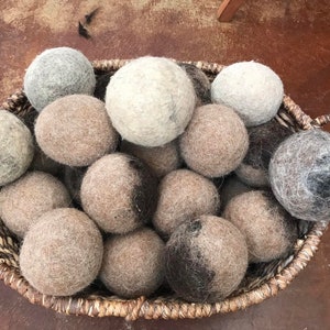May include: A basket filled with a variety of wool dryer balls in shades of gray, brown, and black. The balls are made of felted wool and are designed to help reduce drying time and soften laundry.
