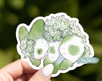 May include: A watercolor sticker of a green and white bunny with a fluffy green mane. The sticker is on a white background and has the text "Ivory Owl Co" in the bottom right corner.