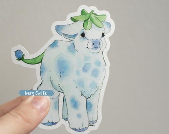 May include: A blue and white watercolor sticker of a cartoon calf with a green leaf crown. The calf has blue spots and a green tail with a blue berry on the end. The sticker is on a white background.